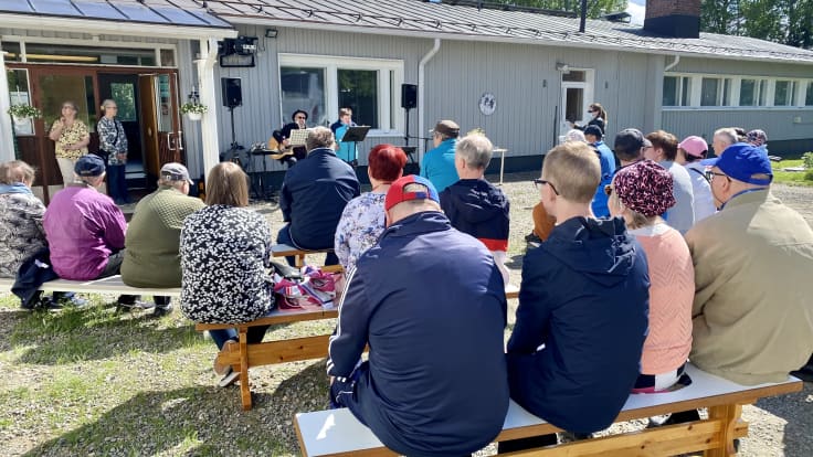 Ihmiset istuvat penkeillä ulkoilmassa kesäjuhlassa kuuntelemassa musiikkiesitystä.