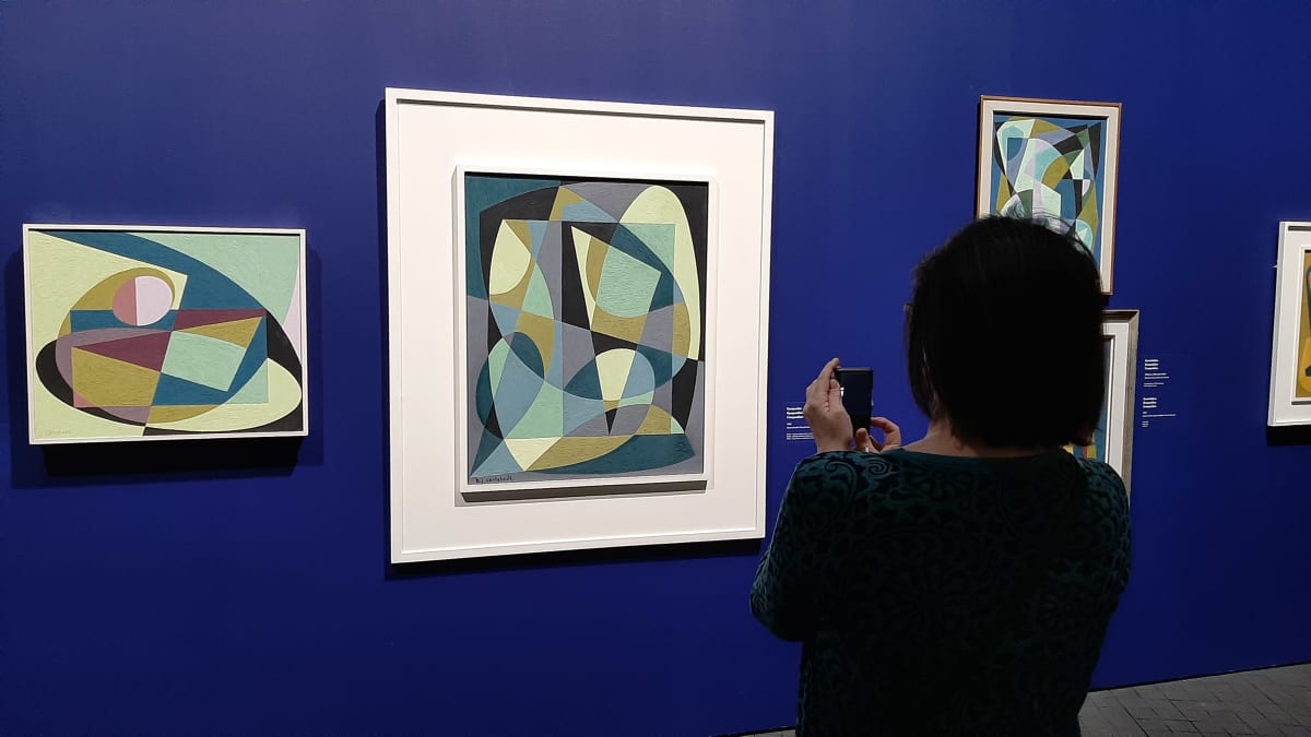 En dam tar ett foto av en nonfigurativ tavla på en utställning.