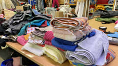Pino värikkäitä pyyhkeitä ja muita tekstiilejä pöydällä.