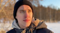Pakkaskeliin pukeutunut Johannes Takamäki katsoo vähän ohi kamerasta. Taustalla luminen järvenranta. Aurinko valaisee puolet kasvoista.