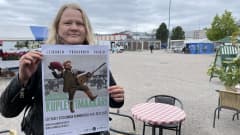 Nainen pitää teatterimainosta käsissään torin laidalla.