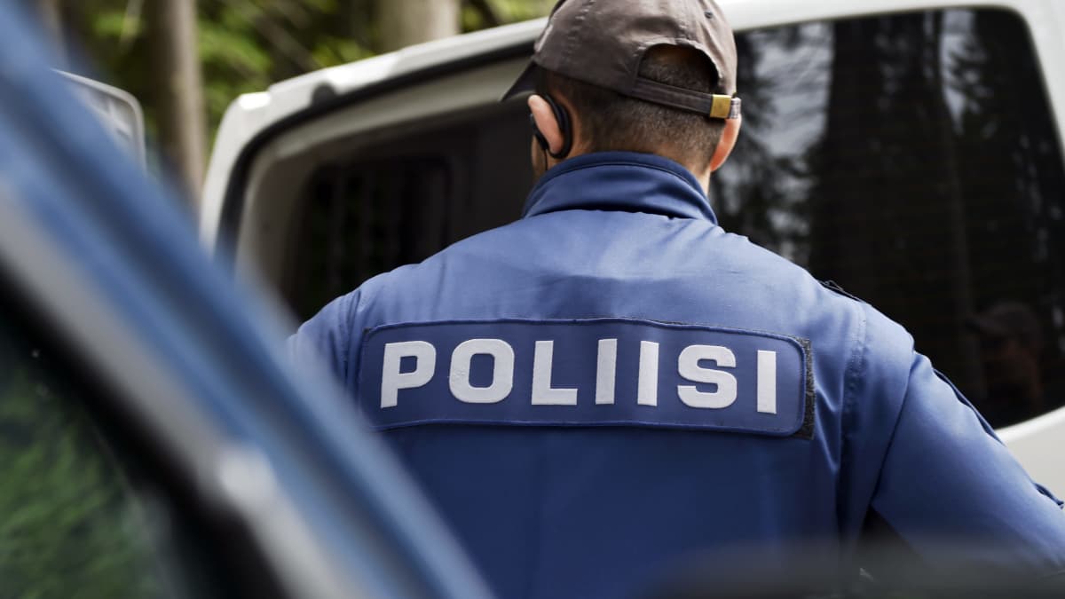 Poliisi seisoo selkä kameraan. Uniformun selässä lukee poliisi.