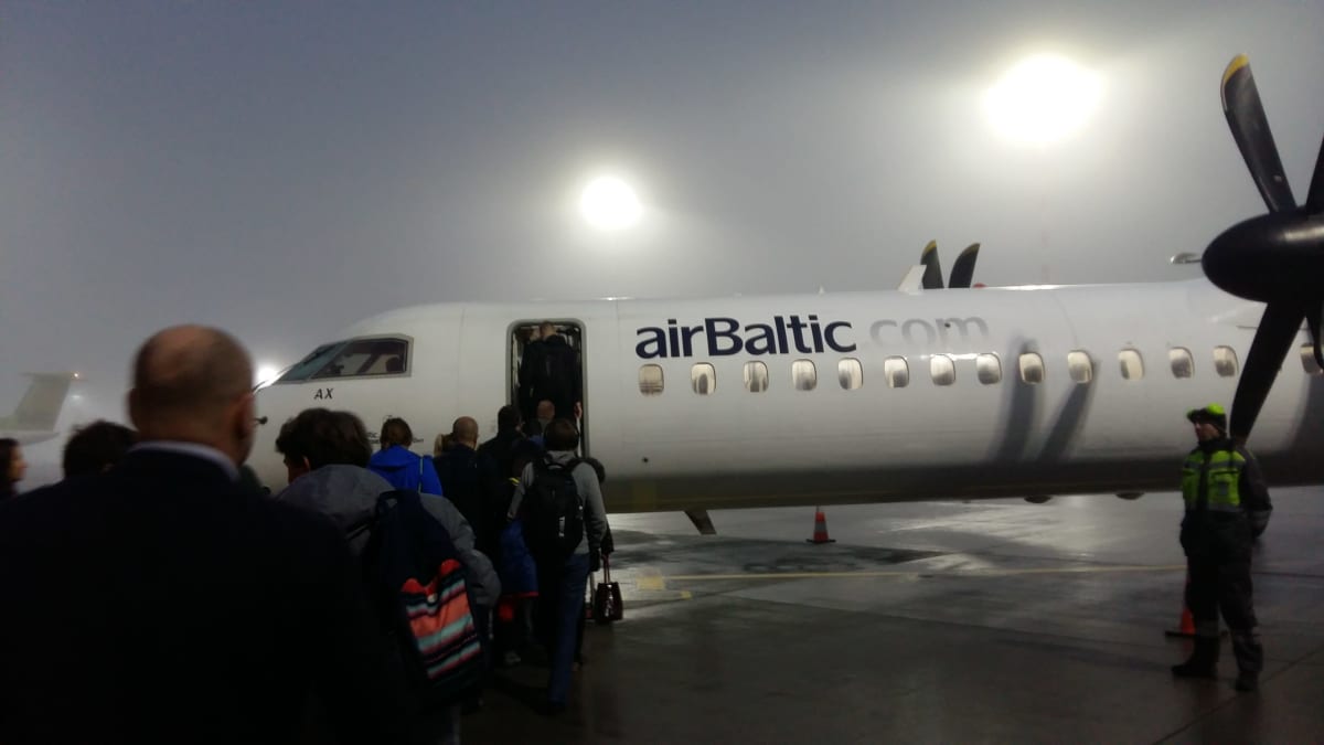 Passagerare vandrar ombord på ett AirBaltic-plan i dimma.