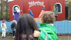 Ett barn i grönturkos regnrock sitter i sin mammas famn och tittar på en teaterföreställning i Muminvärlden i Nådendal.