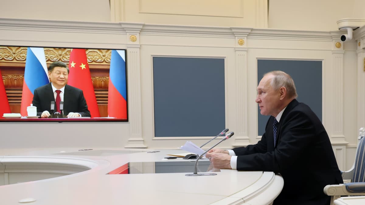 På bilden syns Kinas president Xi Jinping på en stor bildskärm, i förgrunden syns ryska presidenten Vladimir Putin sitta intill ett runt ljust mötesbord med två mikrofoner.