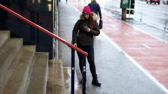 Tyttä talvitakissa ja pipossa lukee puhelinta kadulla.