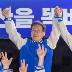Två koreanska män höjer armarna inför en publik.