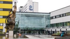 Tampereen yliopistollisen sairaalan pääsisäänkäynti kuvattuna pilvisenä kesäpäivänä. Etualalla suihkulähteitä ja pronssipatsas.