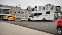 kelta-punainen ambulanssi ajaa tiilirakennuksen ja autojen pysäköuntialueen välissä Oulun yliopistollisen keskussairaalan etualalla. Pysäköintialuella valkoinen matkailuauto.