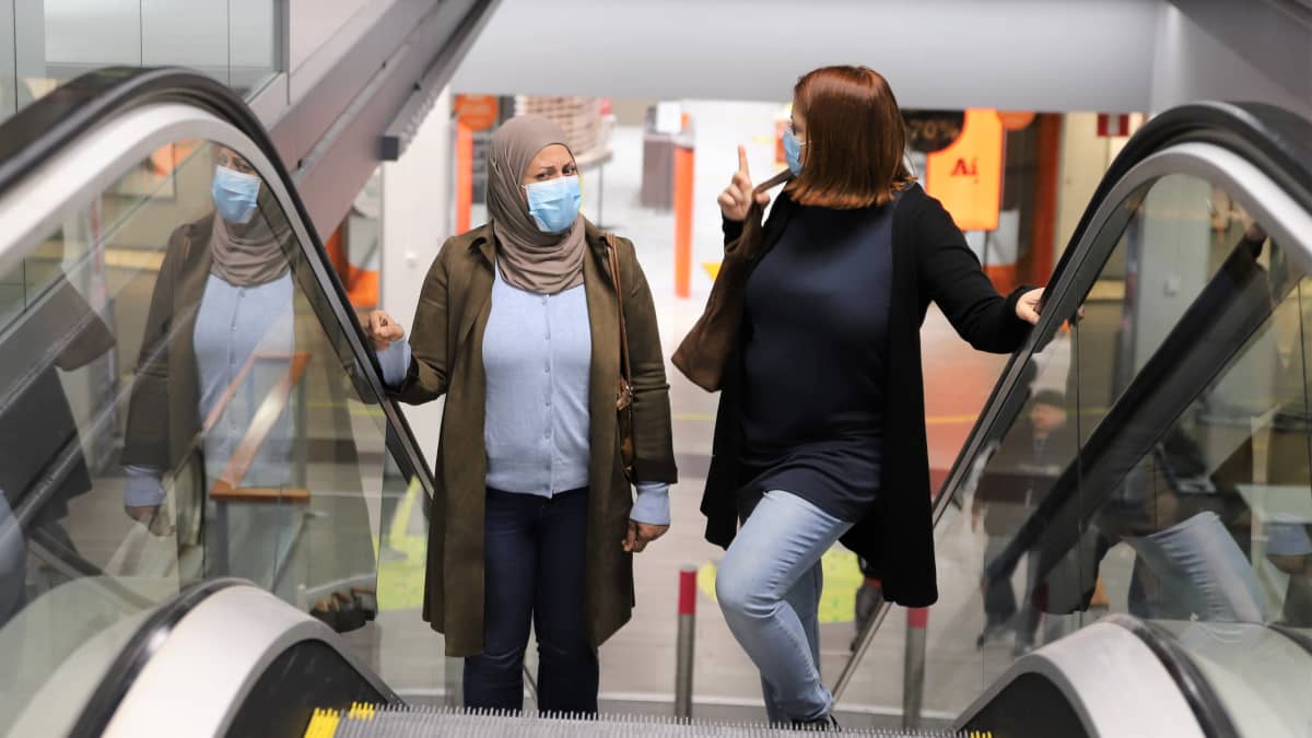 Irakista Suomeen tullut Roqaya Al-Anbagi ja suomalainen Paula Malan seisovat liukuportaissa Trion kauppakeskuksessa Lahdessa.
