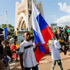 Venäjän lippua kantava mies ja paljon muita ihmisiä kävelee liikenneympyrässä Malissa.