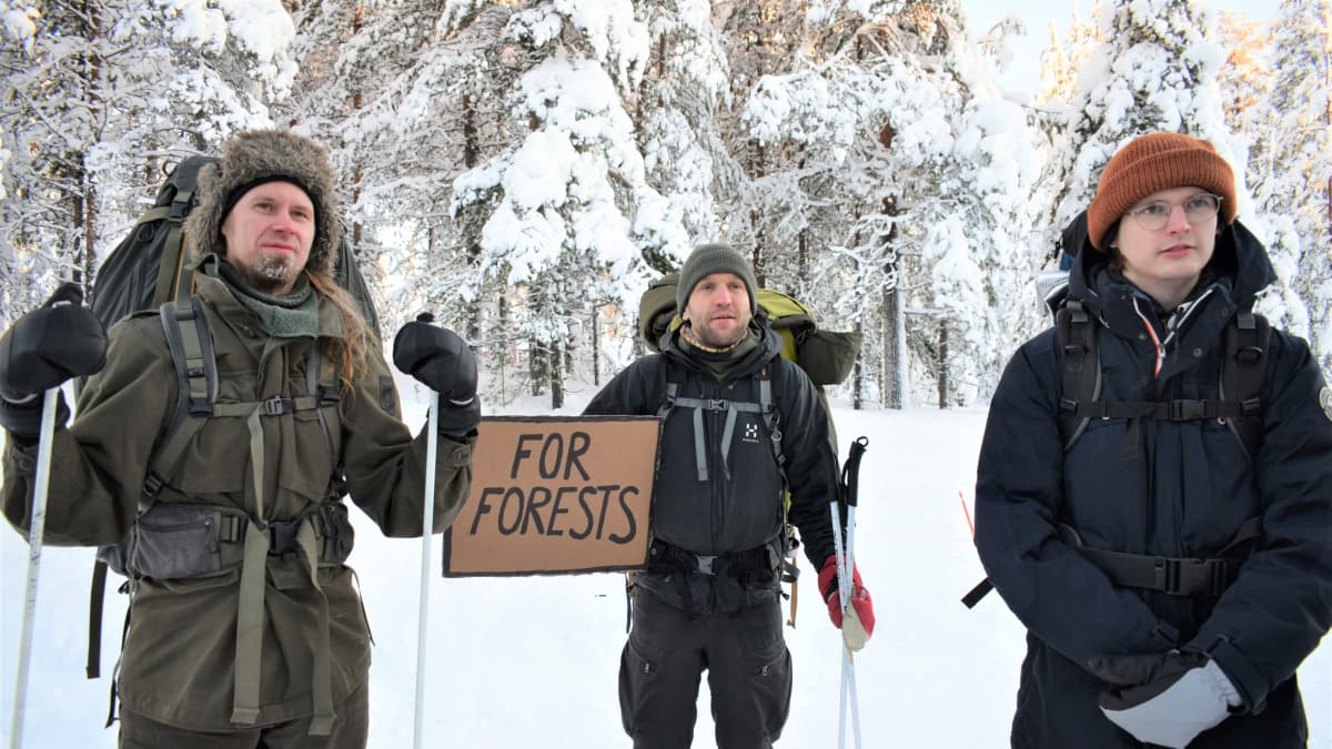 Mielenosoittajia kantamassa kylttiä lumisessa metsässä.