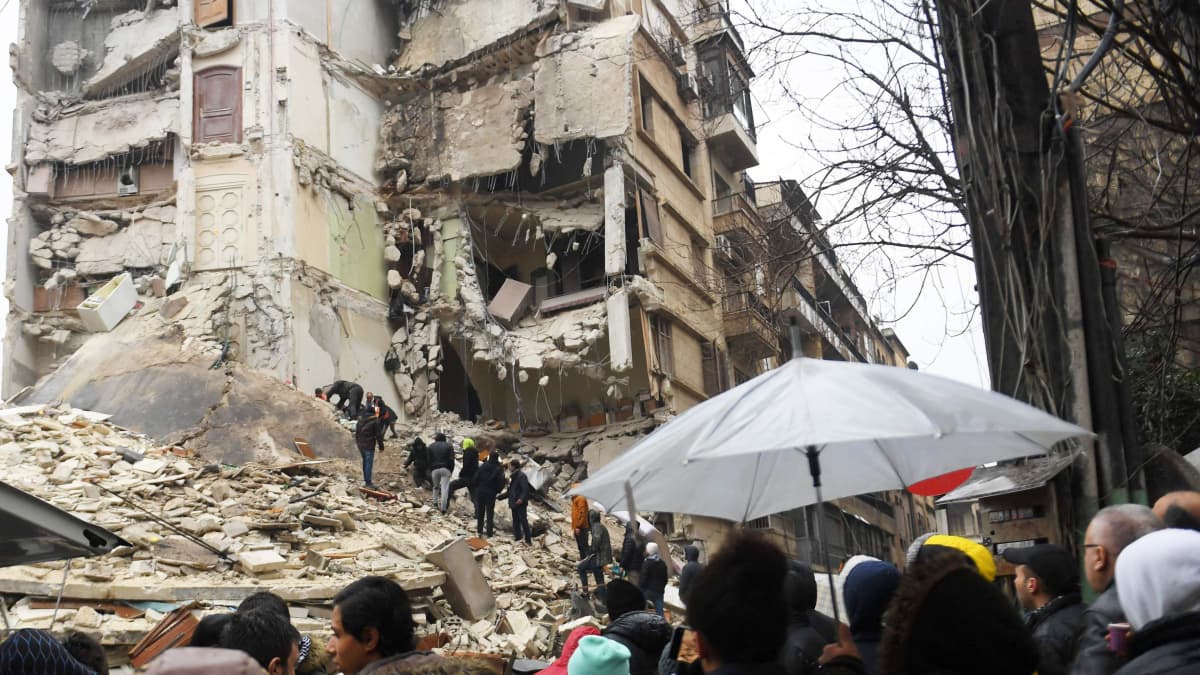 Ihmisjoukko seuraa pelastustöitä romahtaneen asuinrakennuksen vieressä.