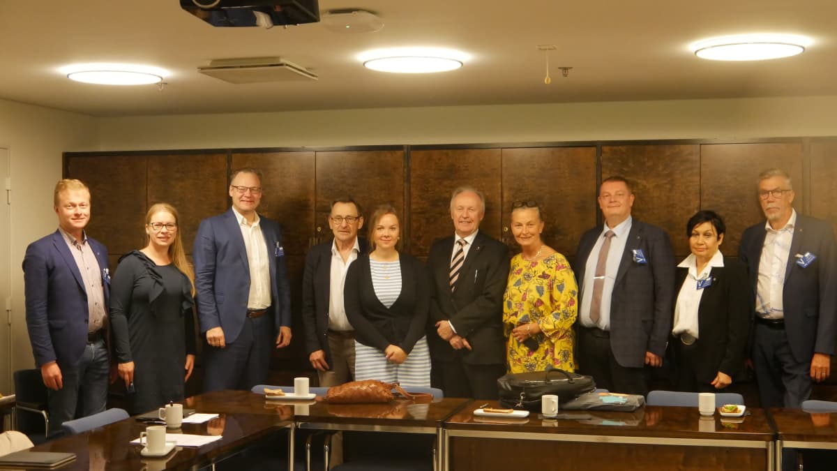 Savonlinnan ja Kemin kaupungin edustajat vierailevat eduskunnassa ministeri Aki Lindénin luona. Kuvassa seisotaan kokoussalin pöydän ympärillä ja katsotaan kameraan.