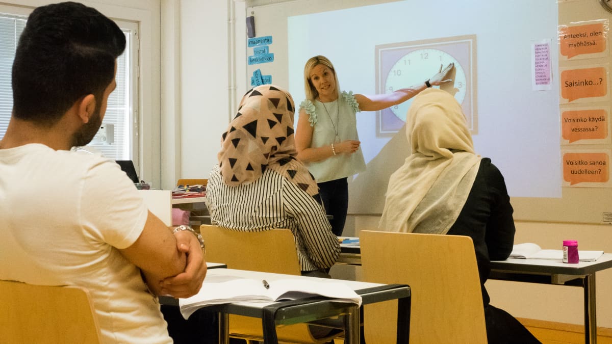 Opettaja näyttää taululta kellonaikoja ja oppilaat katsovat