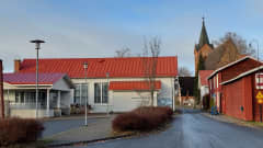 Valkoinen kylätalo, punainen hirsiaitta sekä taustalla kirkon torni.