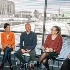 Viisi henkilöä tilapäisessä TV-studiossa. Taustalla ikkunasta näkyy Eduskuntatalo.