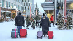 Mies ja nainen vetävät molemmat kahta matkalaukkua perässään lumisessa kaupunkimaisemassa. Kauempana kolmen hengen perhe.