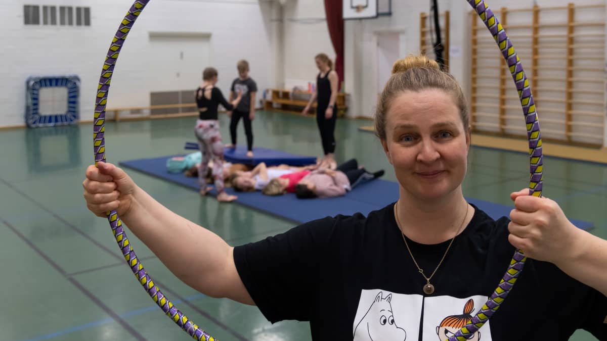Nainen pitää hulavannetta käsissään, takana sirkuskoulun oppilaita.