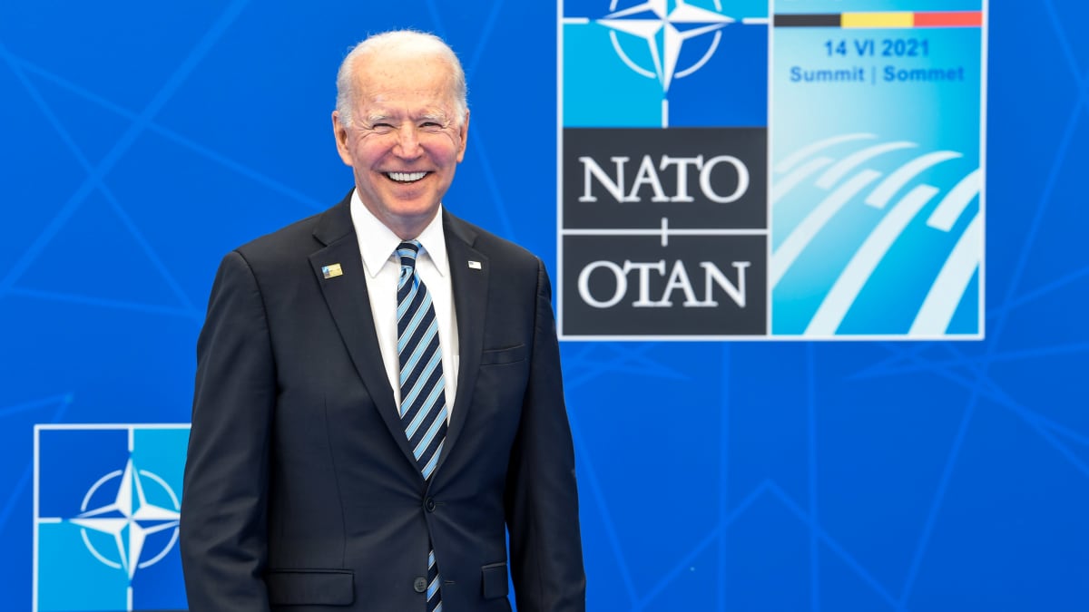 Joe Biden naureskelee iloisesta, taustalla Nato huippukokouksen juliste. 