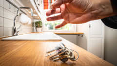 Käsi pudottaa asunnon avaimet keittiötasolle.