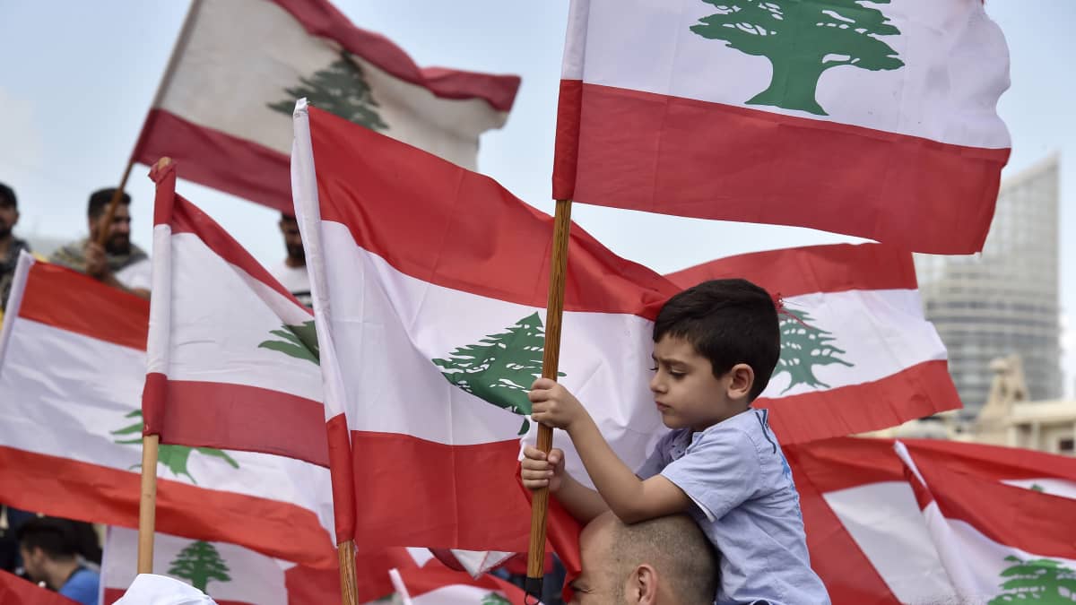 Miehen hartioilla istuva poika pitelee Libanonin lippua.