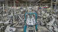 Photo shows a large vehicle factory, filled with robotics and parts of vehicles on assembly lines.