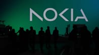 Silhouettes of about a dozen people in front of a large dark-green wall sign with the stylised word NOKIA. 