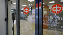 Kuva pankin ovesta, jossa osuuspankin logot. Ikkunasta heijastuu katumaisema.