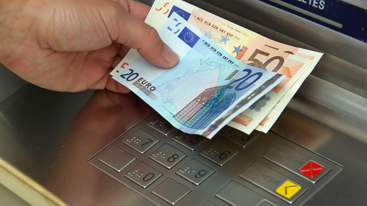 Henkilö pitää kädessään euroseteleitä pankkiautomaatilla.