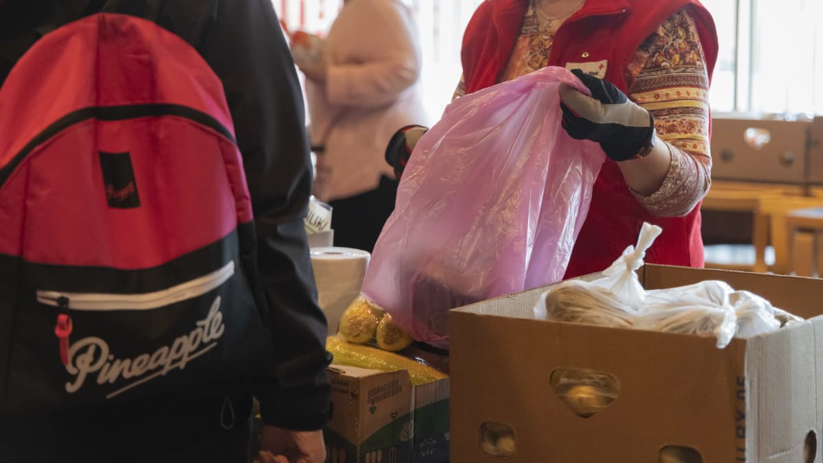 Suomen Punaisen Ristin vapaaehtoinen antaa ruokajonossa olevalle henkilölle elintarvikkeita.