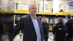 Energon myyntipäällikkö Mikko Summala katsoo kohti kameraa, taustalla Energon logo-takki päällä olevia työntekijöitä ja keltainen Föli-bussi.