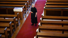 Nainen kirkon keskikäytävällä papin vaatteissa.