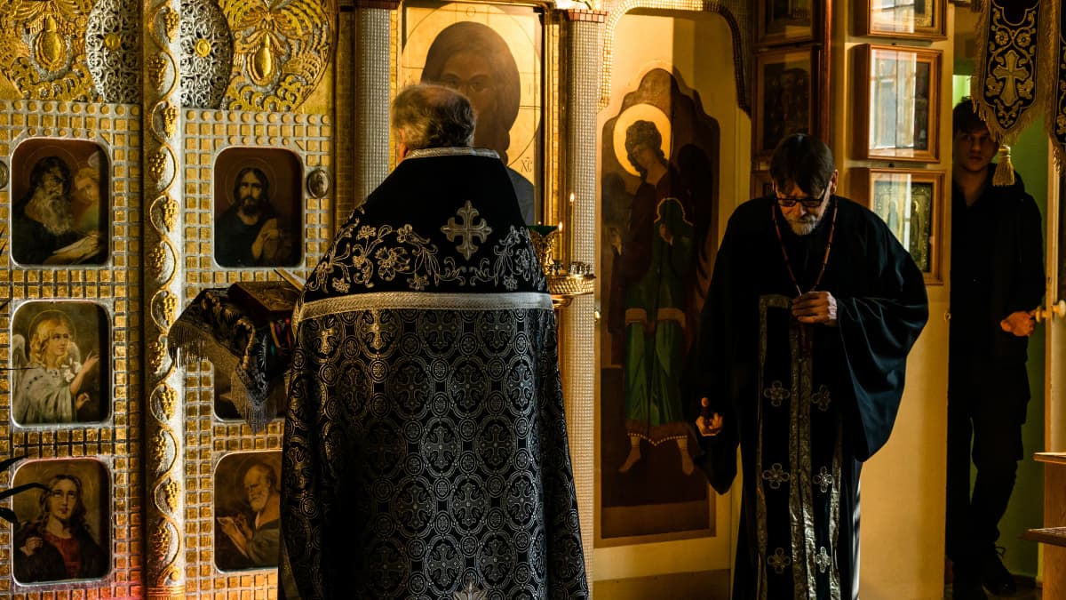 Ortodoksisen kirkon jumalanpalvelusta vetävä pappi kääntyneenä selin alttarin edessä.