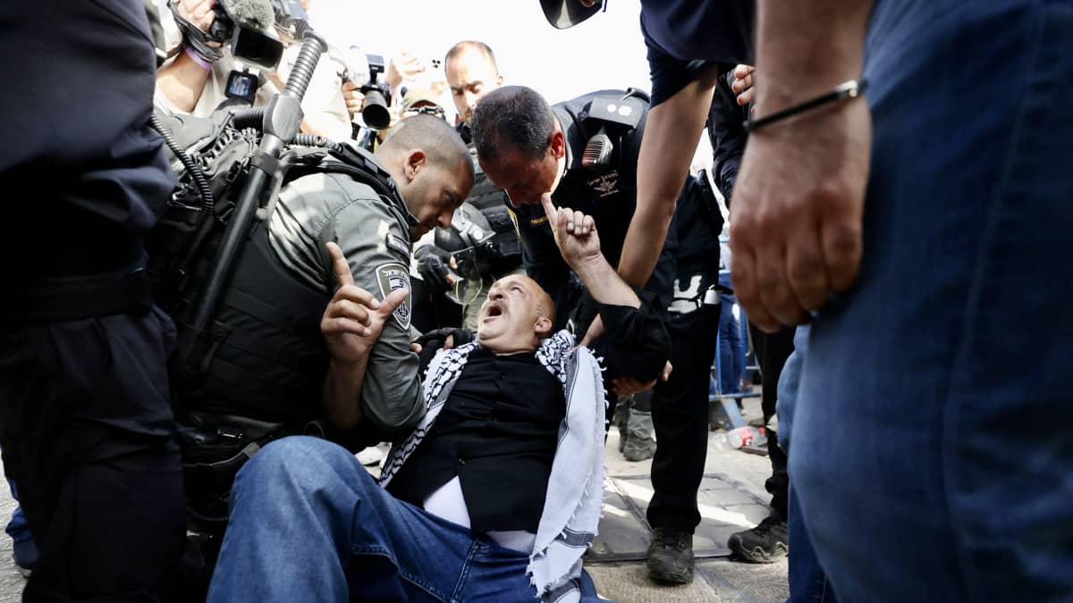 Poliisi nostaa maasta miestä, jonka hartioille on sidottu palestiinalaishuivi.