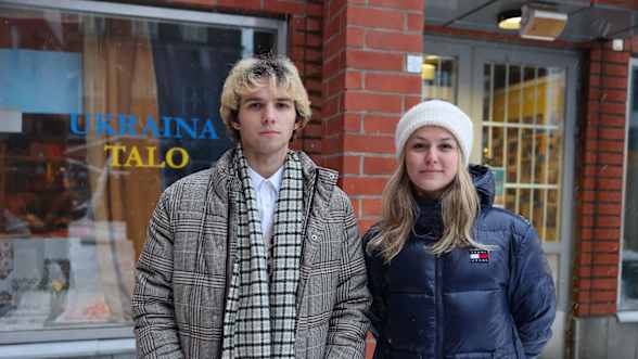 Nuori ruudulliseen takkiin pukeutunut mies ja siniseen takkiin pukeutunut nainen katsovat kameraan. Taustalla Tampereen Ukraina-talo.