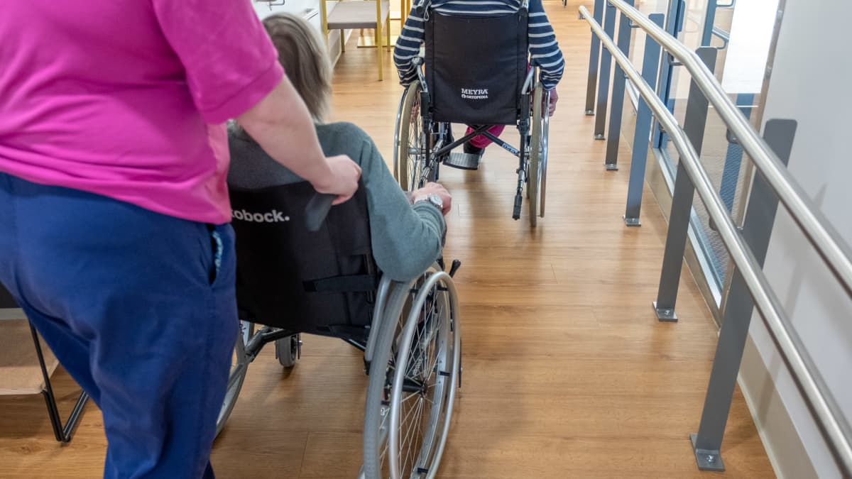 Hoitaja työntää vanhusta pyörätuolissa.
