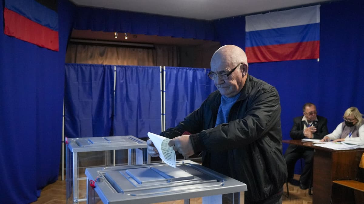 En man lägger en röstsedel i en urna. I bakgrunden den ryska flaggan.
