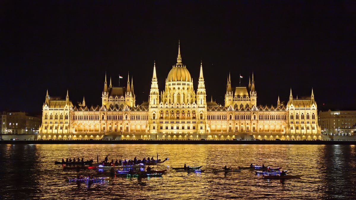 Unkarin parlamenttitalo kirkkaasti valaistuna pimeässä illassa.