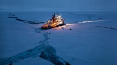 Kirkkaasti valaistu tutkimusalus tummenevalla jäisellä merellä, jossa kelluu jäälauttoja. 