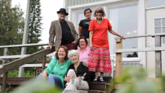 Viisi naista ja yksi mies istuu tai seisoo talon portailla ja hymyilee kameralle elokuun pilvipoutaisessa säässä.