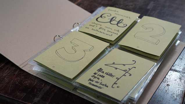 En mapp ligger uppslagen på ett bord. I mappen finns plastfickor med numrerade kort.