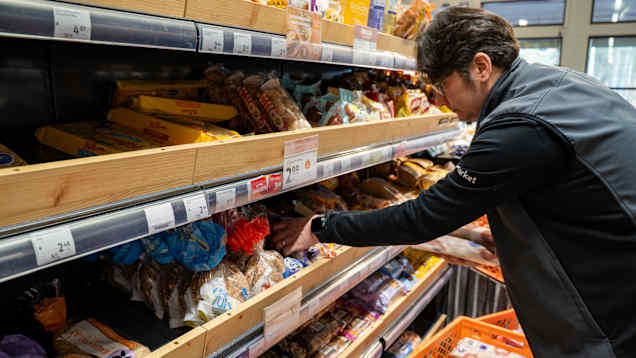 En man som lägger upp bröd på en hylla i en matbutik. 