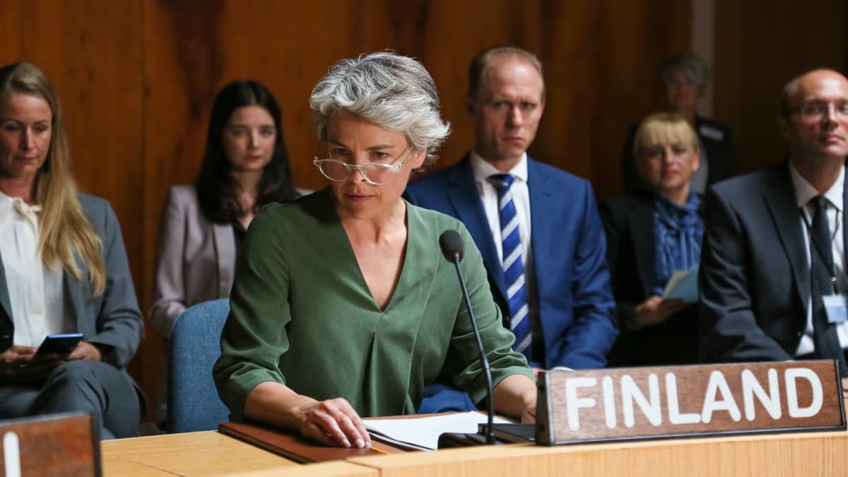 Ann-Mari Sundell (Irina Björklund) istuu vakavana rauhanneuvottelusalissa takanaan ihmisiä.
