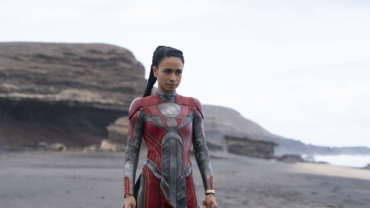 Eternals-elokuvan supersankari Makkari eli näyttelijä Lauren Ridloff punaisessa supersankariasussaan kivisellä rannalla.