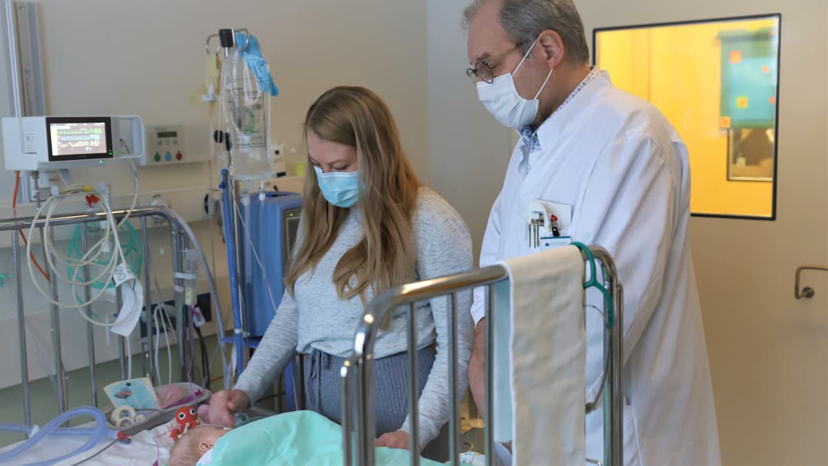 Pieni vauva lepää sairaalasängyssä. Monitori seuraa hengitystä. Vierellä vauvan äiti ja lääkäri.