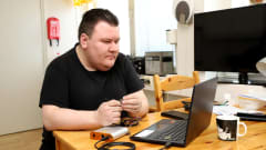 Jussi Koskenkorva istuu pöydän äärellä tietokoneen edessä, kädessä pöydällä olevasta laitteesta tulevia johtoja.