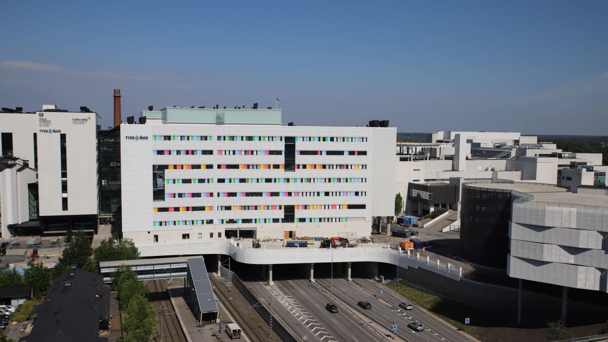 Valkoinen sairaalarakennus moottoritien päällä, värikkäitä yksityiskohtia ikkunoiden vieressä
