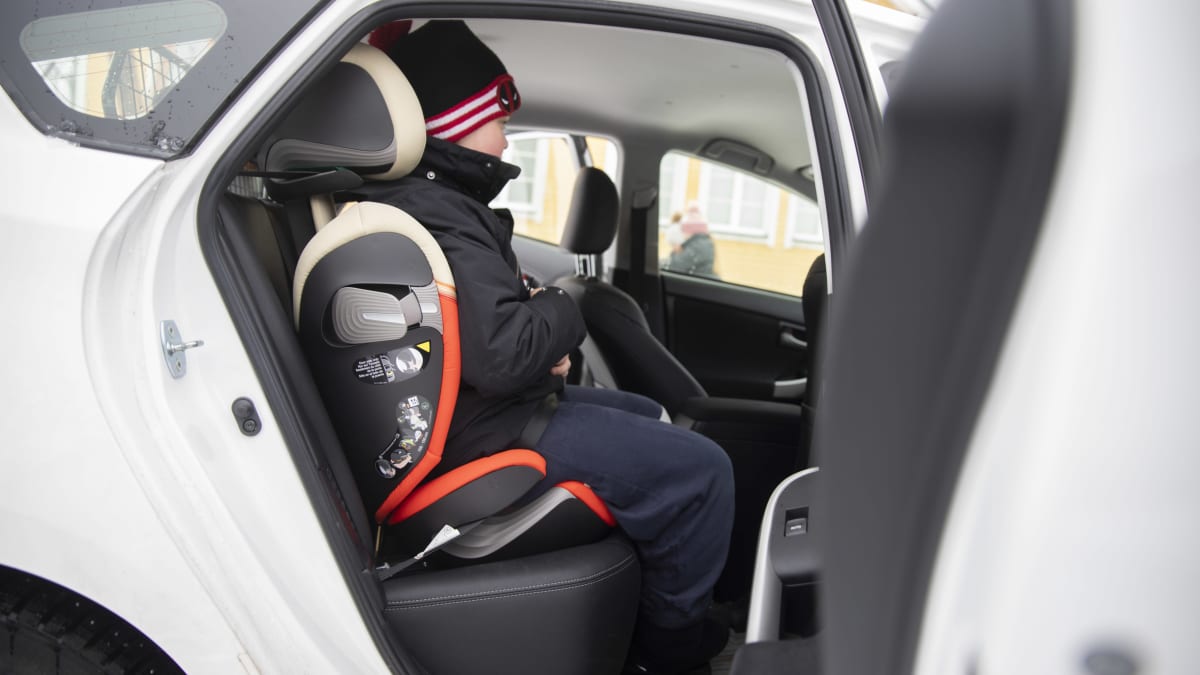 Kouluikäinen lapsi istuu turvaistuimessa pysäköidyn henkilöauton kyydissä.