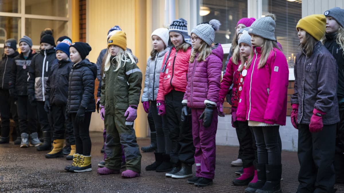 Lapset seisovat rivissä koulun pihalla. 